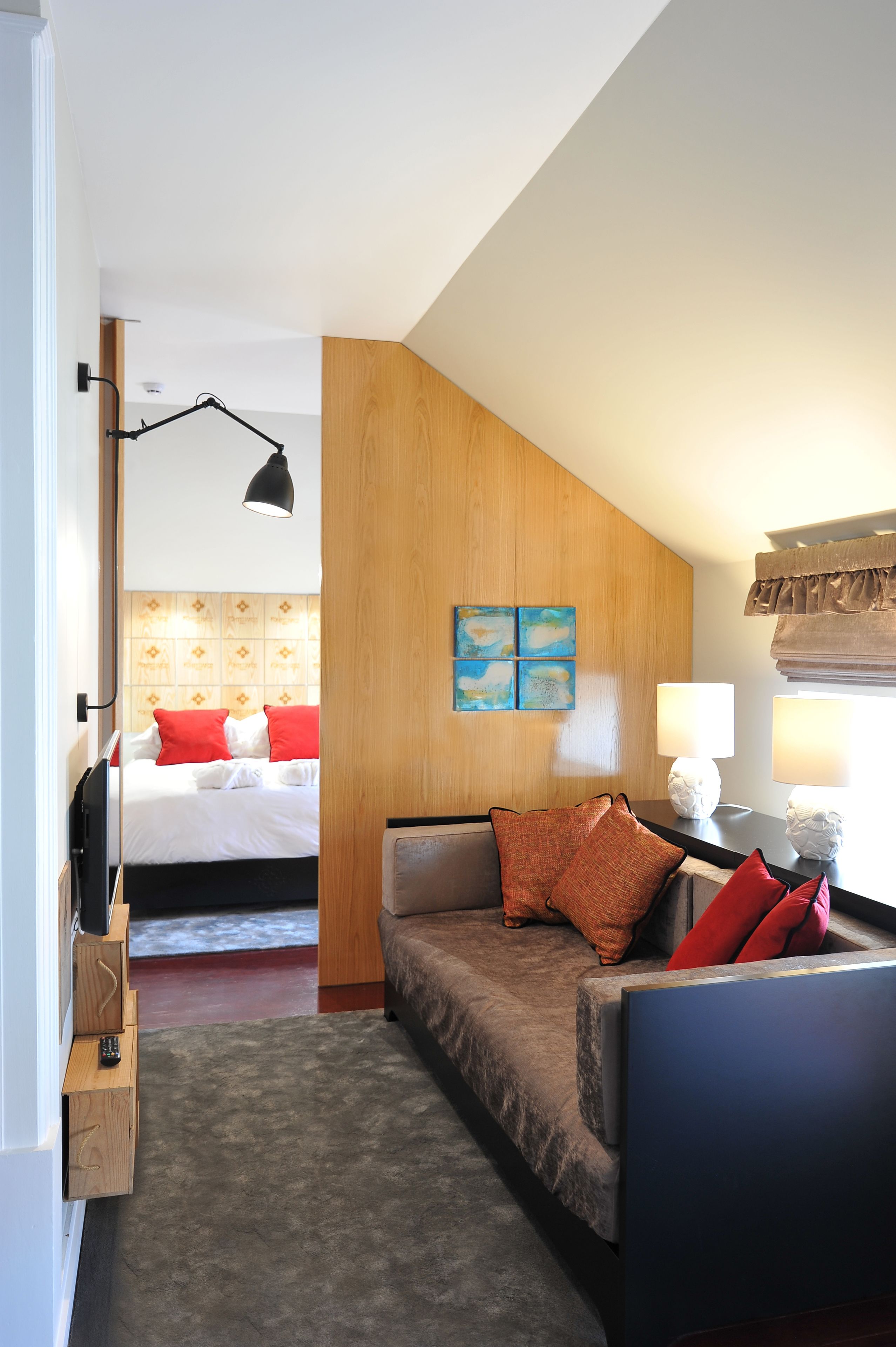 A hotel room with a bed, a sofa, a lamp, and a painting on the wall.
