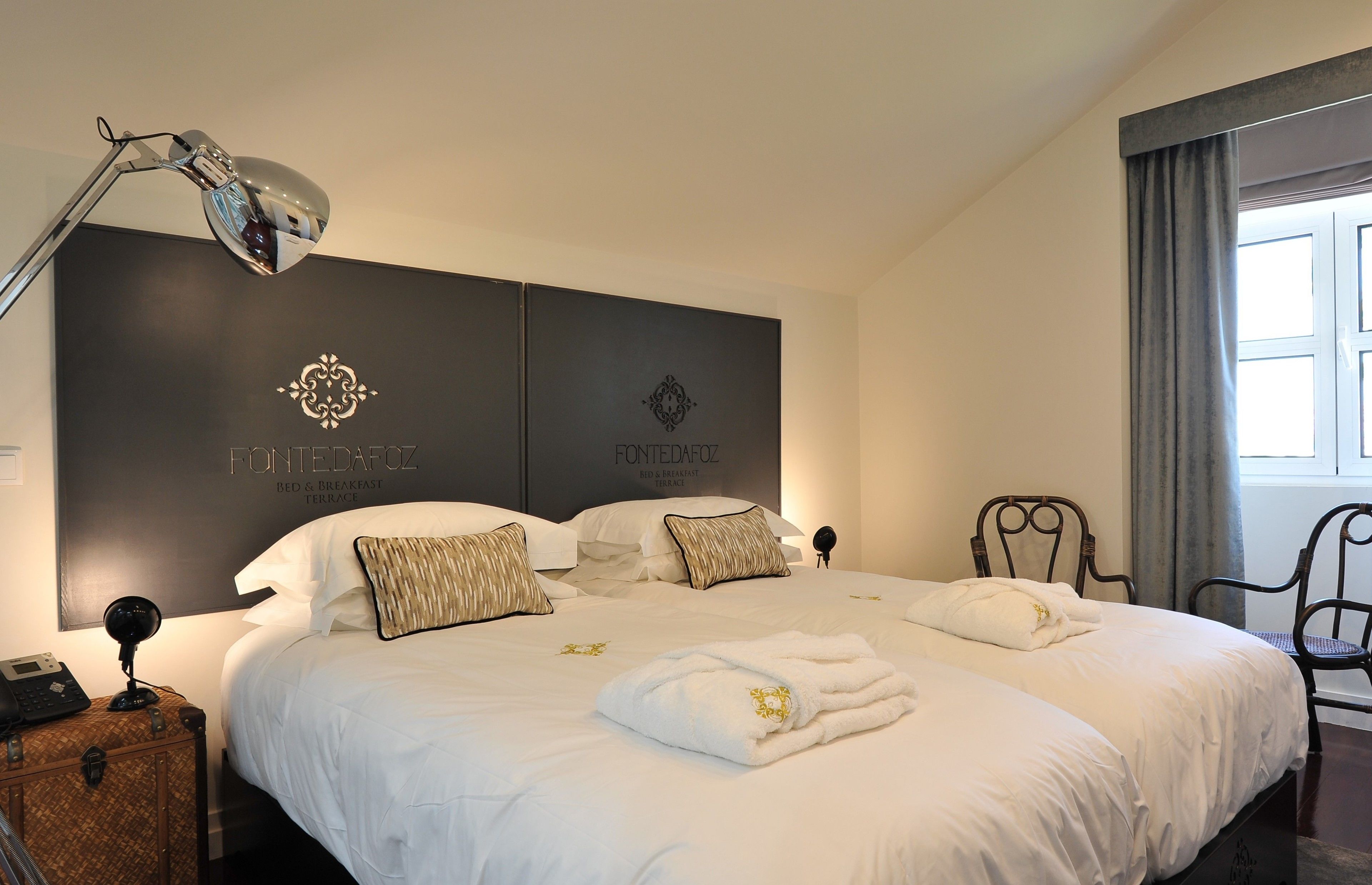 Habitación de hotel con una cama grande, un escritorio con lámpara y una silla. Hay una ventana con cortinas y un cartel en la pared.