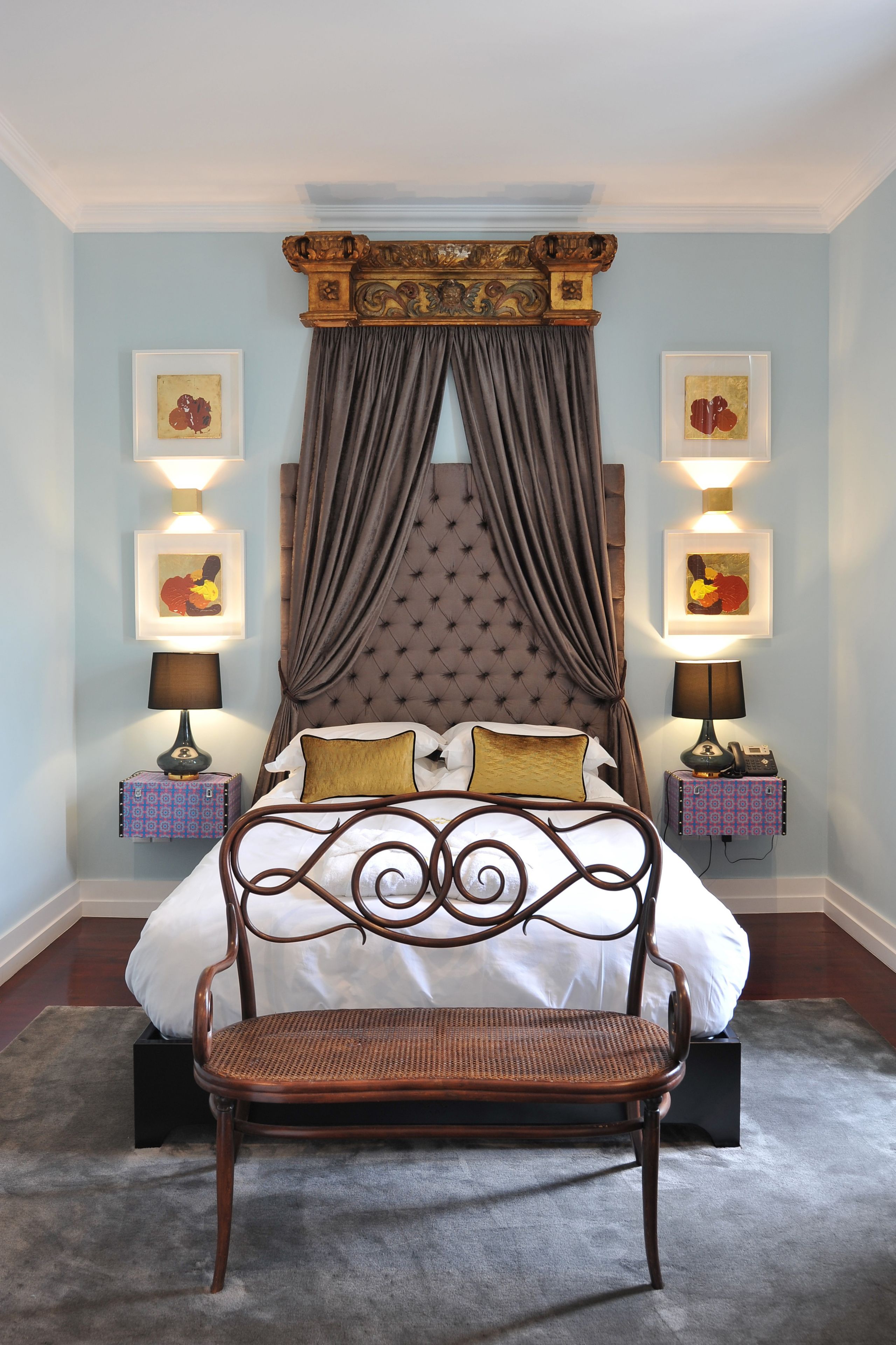 Une chambre à coucher avec un lit à baldaquin, un fauteuil en rotin et deux tables de chevet ornées de lampes et de tableaux encadrés.