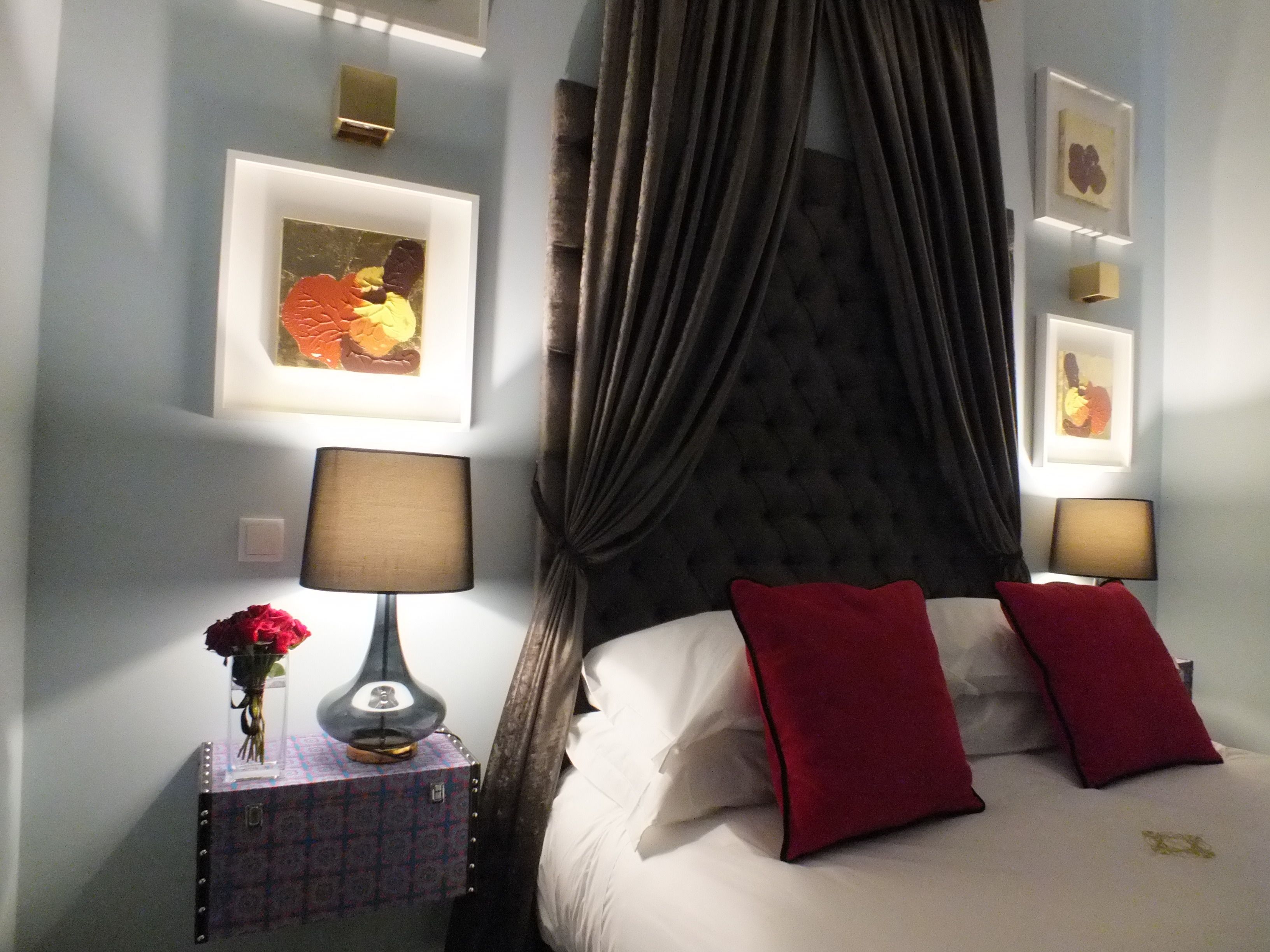 Un dormitorio ordenado con una cama, una mesita de noche con lámpara y una obra de arte en la pared.