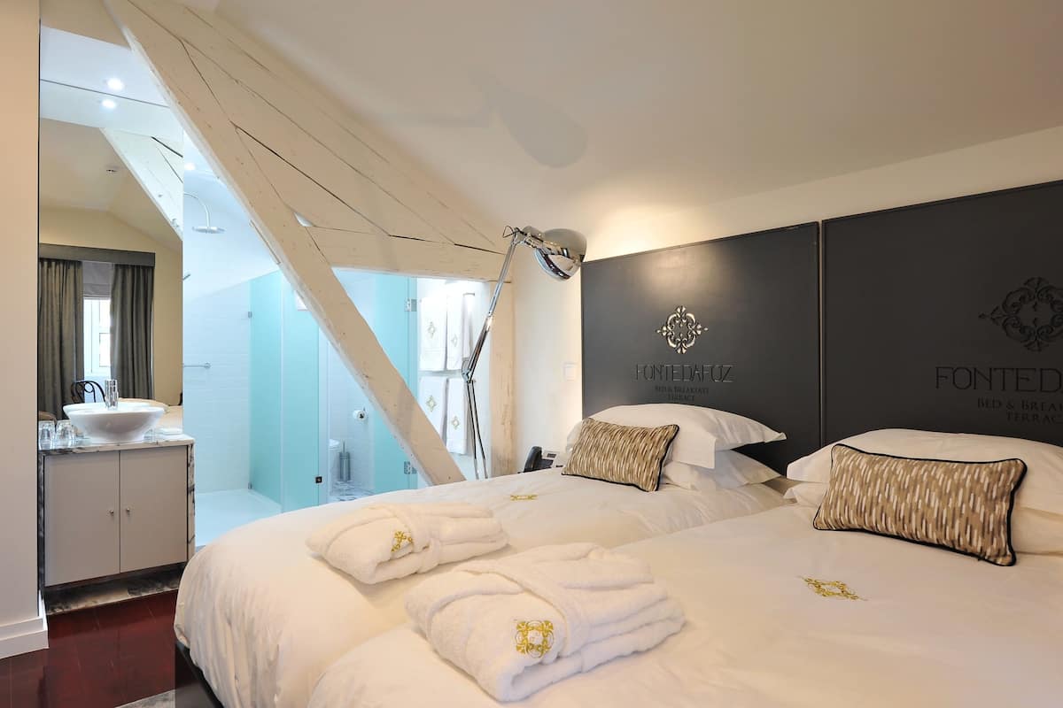 A modern hotel room with a large bed, a bathroom with a glass shower, and a view of the outside.