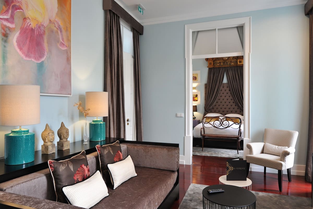A modern hotel room with a sofa, armchair, and a bed with a headboard.