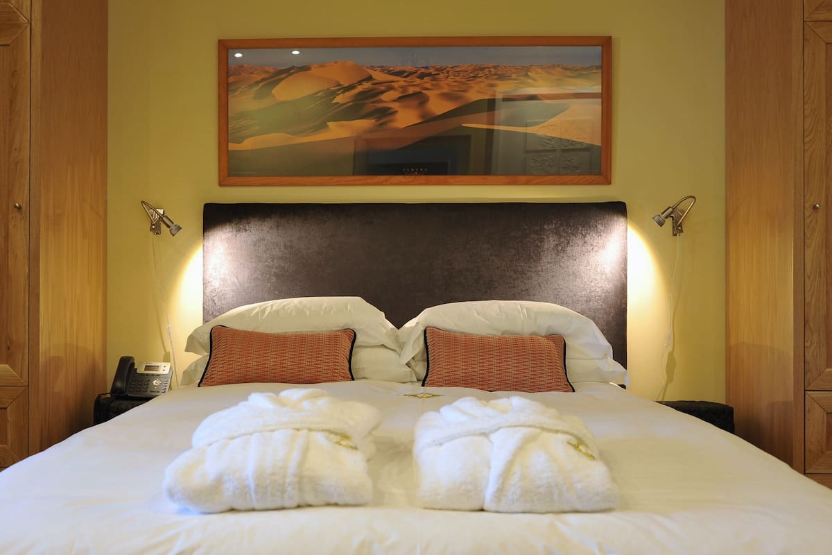 A neatly made bed with two towels, a painting of a desert landscape above it, and wooden cabinets on either side.