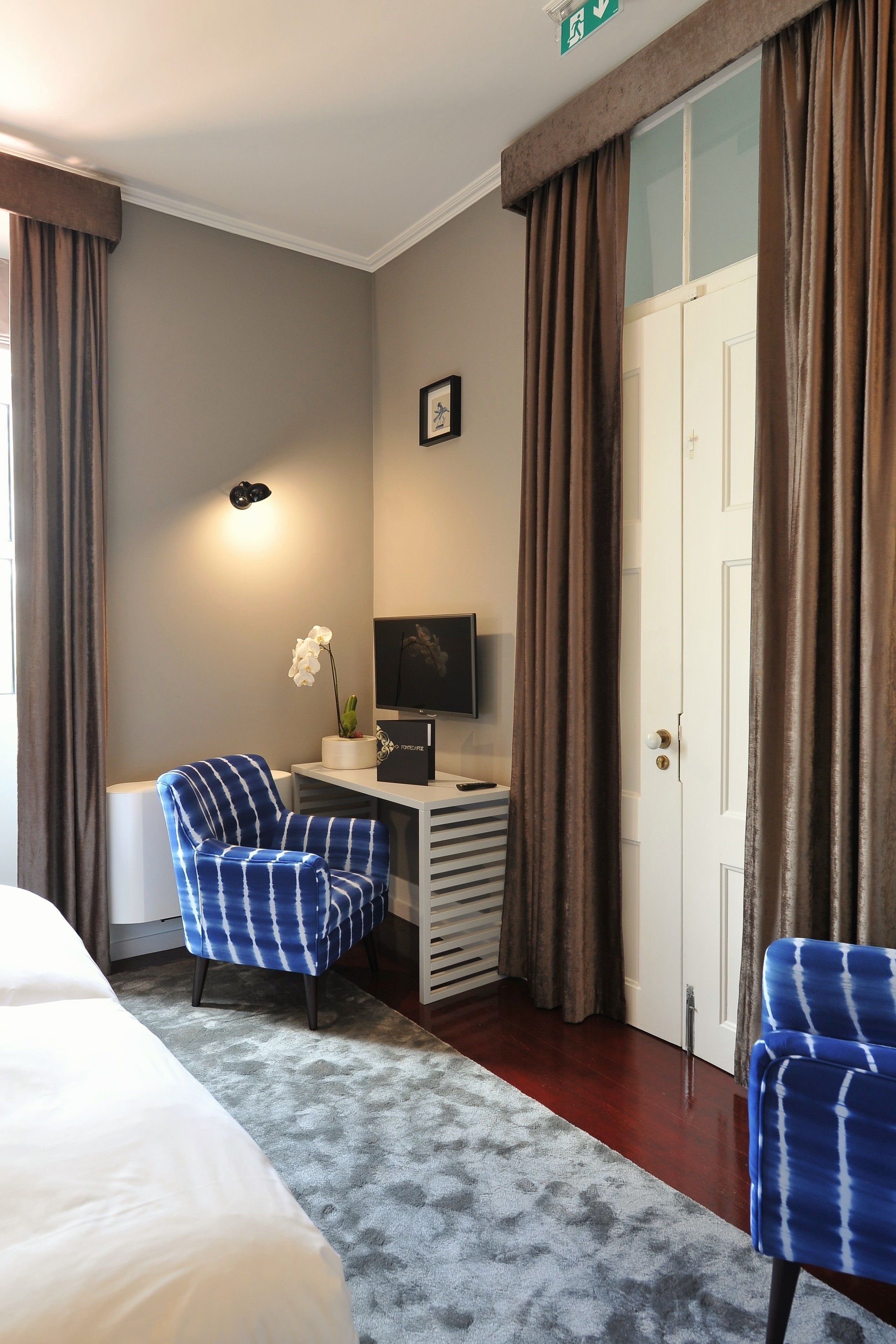 A hotel room with a bed, a desk with a computer, two chairs, a TV, and a door.