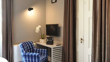 A hotel room with a bed, a desk with a computer, two chairs, a TV, and a door.