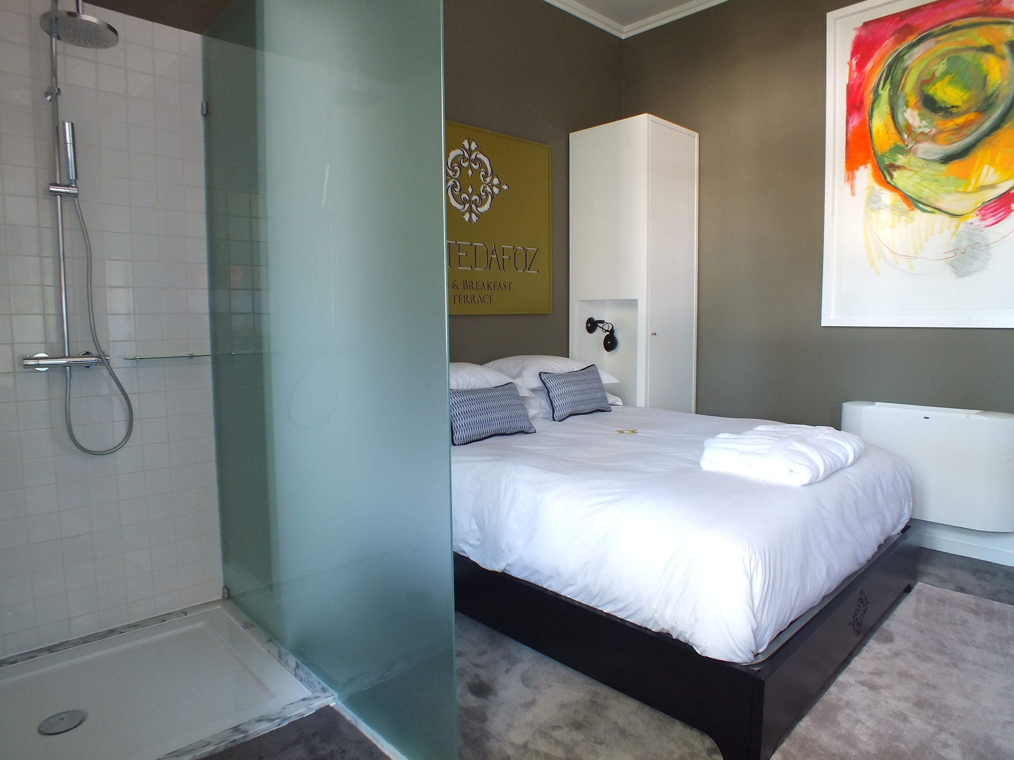Uma casa de banho moderna com cabine de duche em vidro, sanita branca e cama com roupa de cama branca.