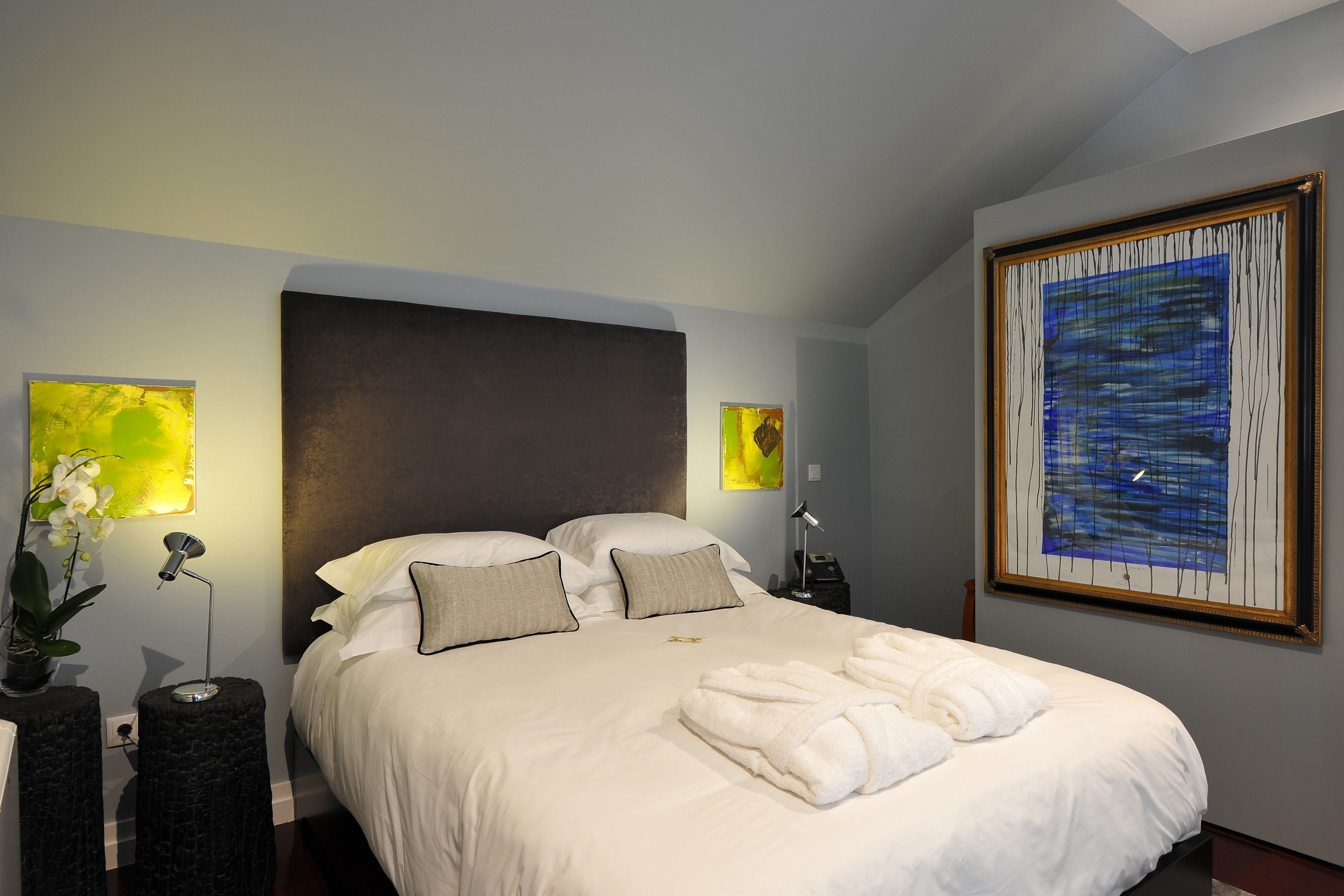 A hotel room with a large bed, two bedside tables, a nightstand, and a painting on the wall.