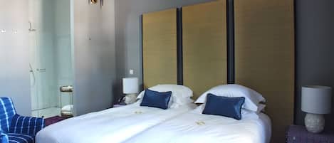 Habitación de hotel con una cama grande, dos mesitas de noche, una silla, un espejo y zona de ducha.