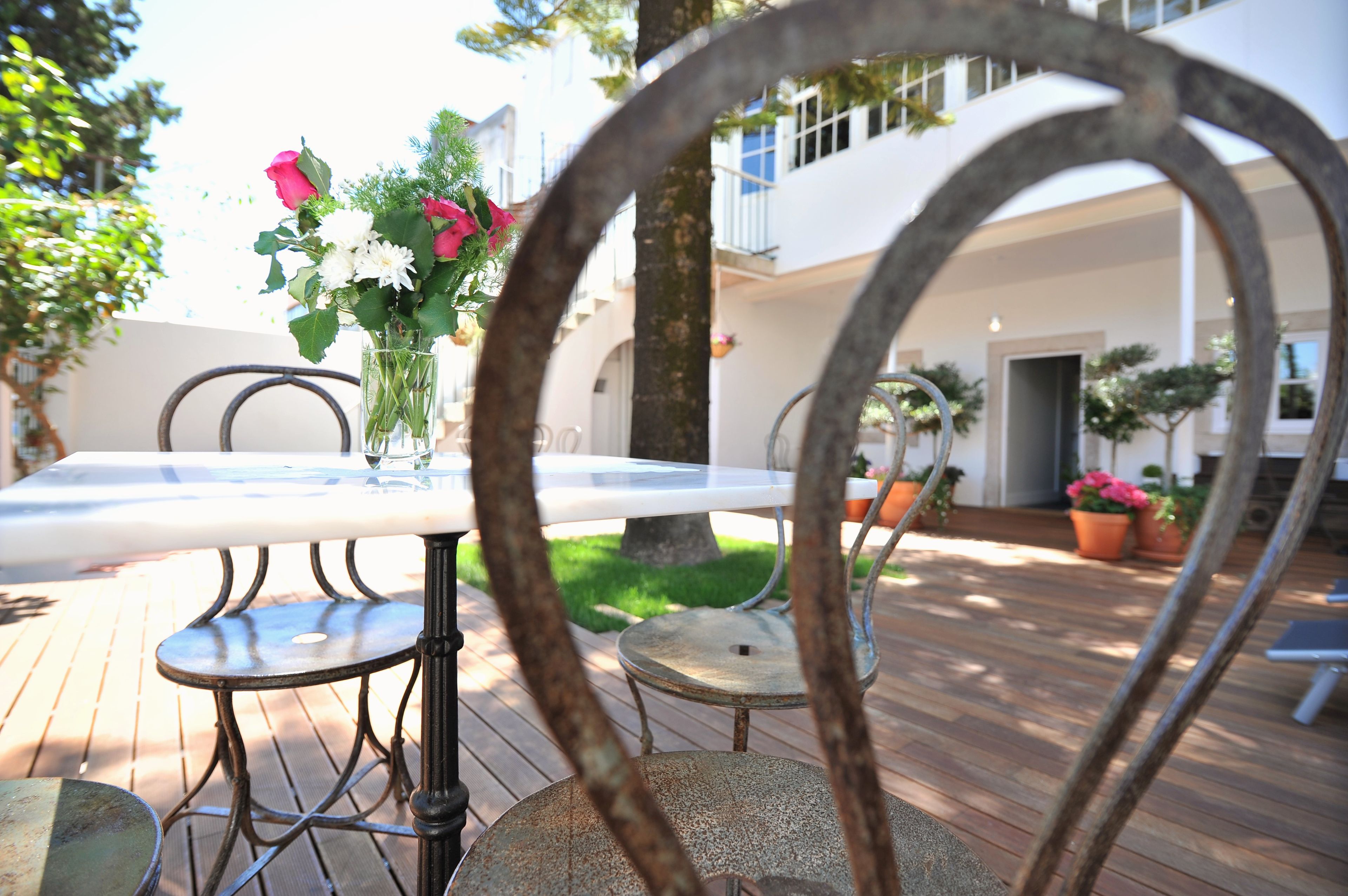 A patio with a table and chairs, surrounded by potted plants and a building in the background.