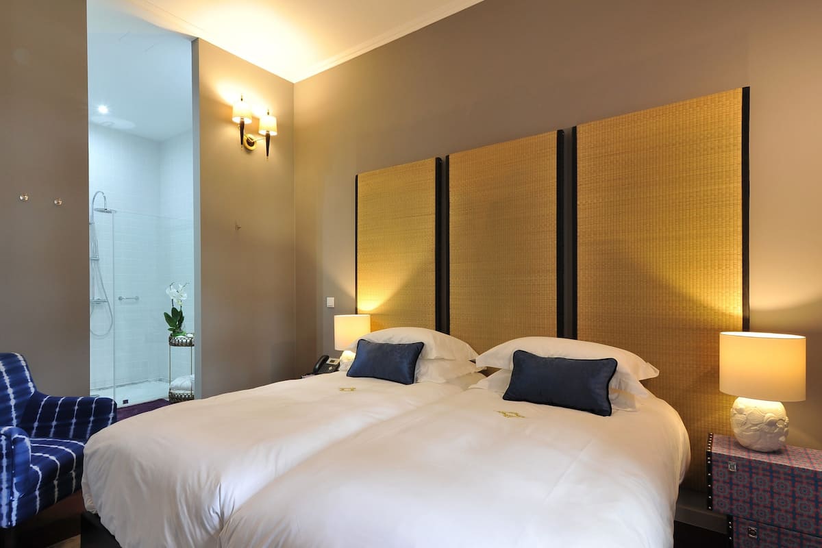 A hotel room with a large bed, two bedside lamps, a nightstand, a chair, and a shower area.
