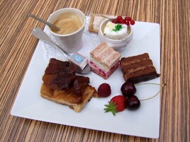 Un plato con diversos postres, incluyendo una porción de tarta, un sándwich y una taza de café.