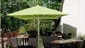 Un espace extérieur aménagé en terrasse, avec des meubles en osier et un parasol vert.