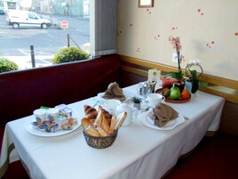 Una mesa de desayuno con croissants, pan, frutas y bebidas, en una habitación con vistas a la calle.