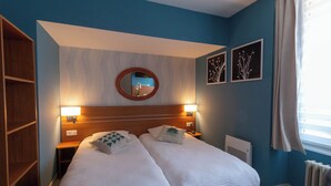 Quarto de hotel com duas camas, cabeceira de madeira, espelho redondo e decoração na parede.
