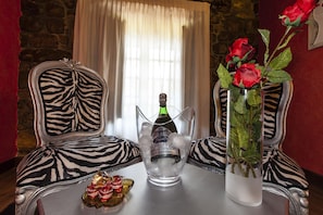 Quarto com cadeiras em padrão de zebra, uma mesa com uma garrafa de champanhe, um vaso com rosas vermelhas e um prato decorativo.