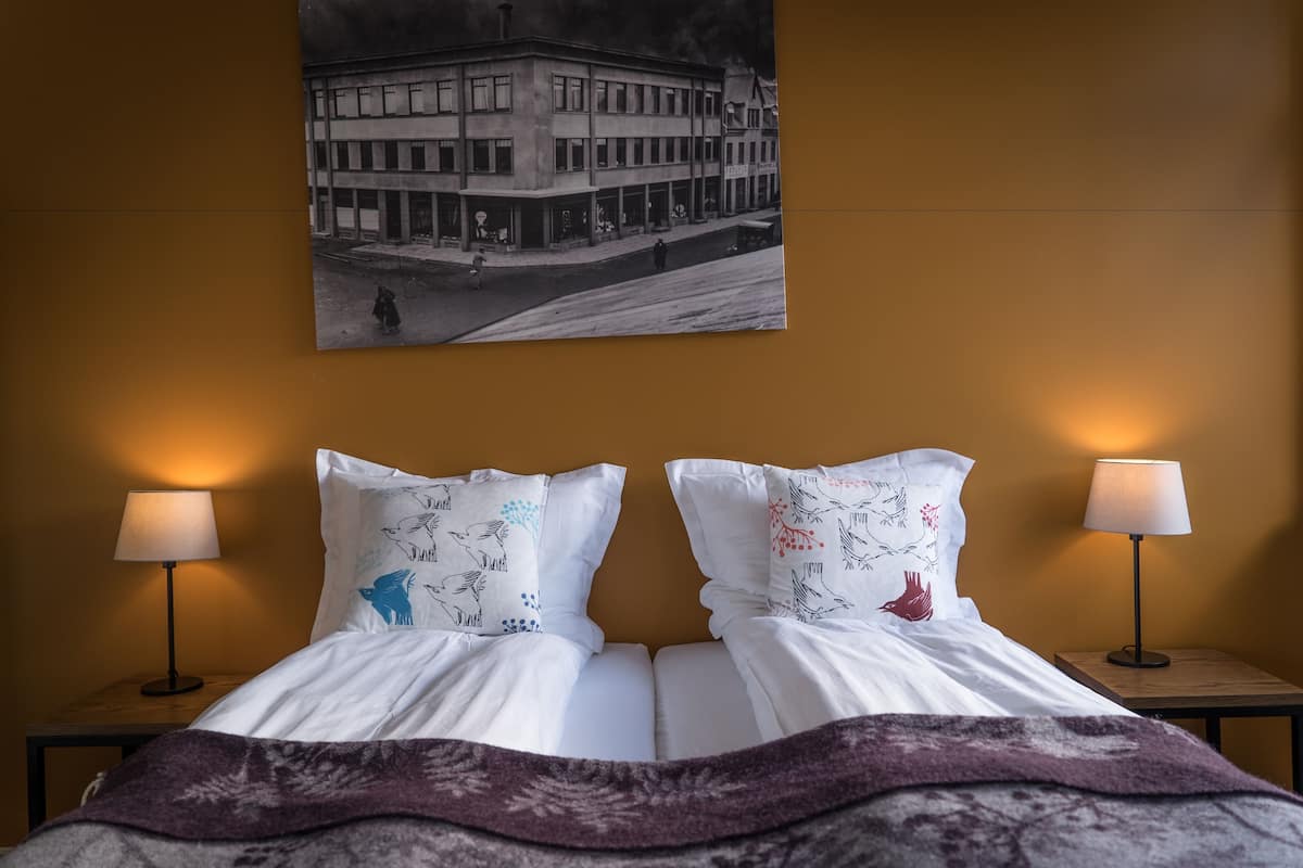 A hotel room with a bed, two bedside lamps, and a wall-mounted picture of a building.