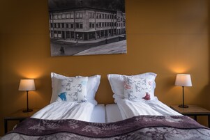 Una habitación de hotel con una cama, dos lámparas de noche y un cuadro en la pared de un edificio.