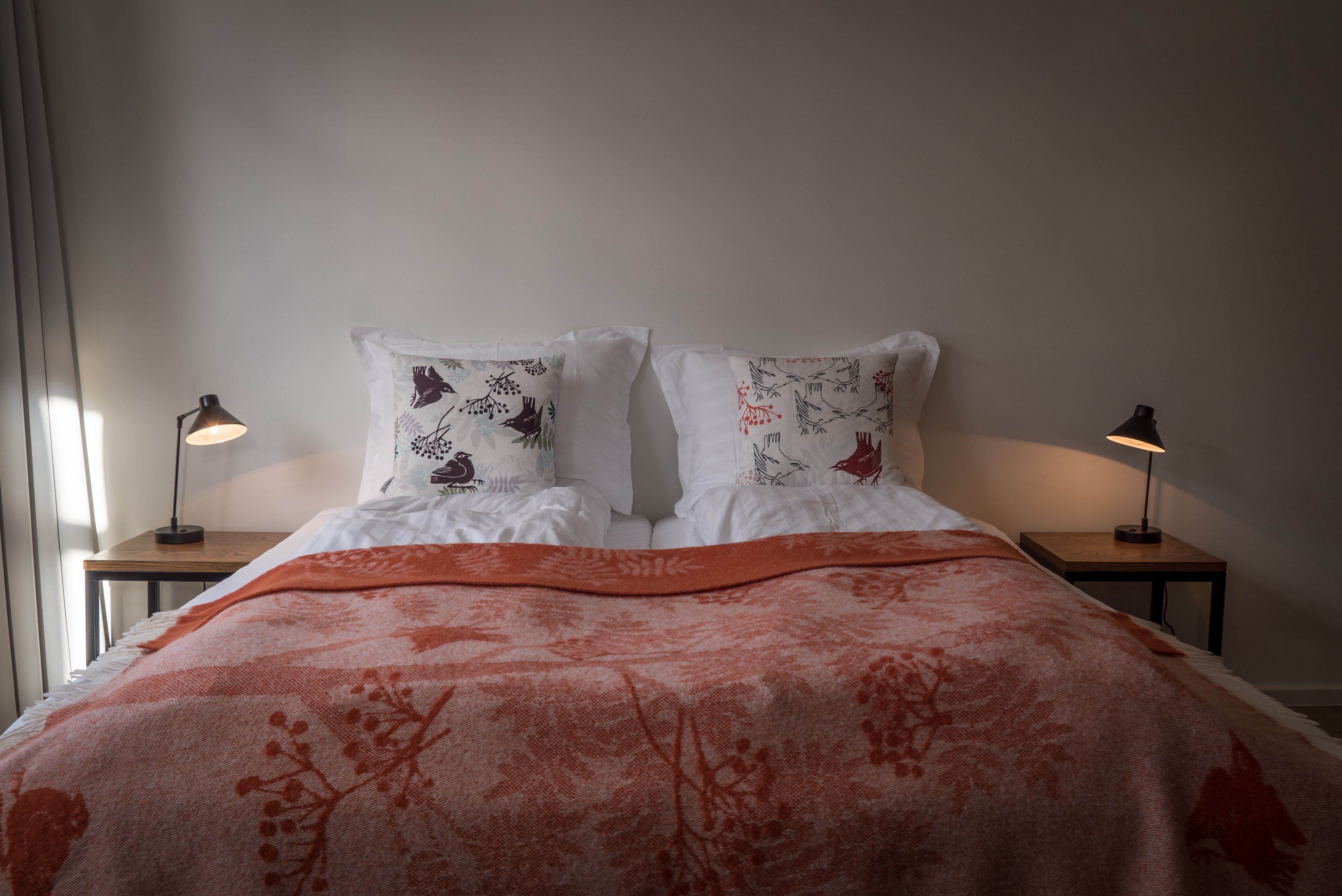 A neatly made bed with a patterned blanket, two pillows with floral designs, and two bedside lamps on wooden nightstands.