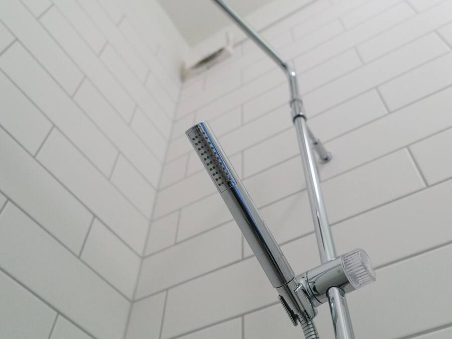 Una doccia con soffione a mano e soffione a parete in un bagno piastrellato.