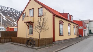 Un edificio de dos plantas con techo rojo y paredes color beige, una valla de madera y una bicicleta estacionada adelante.