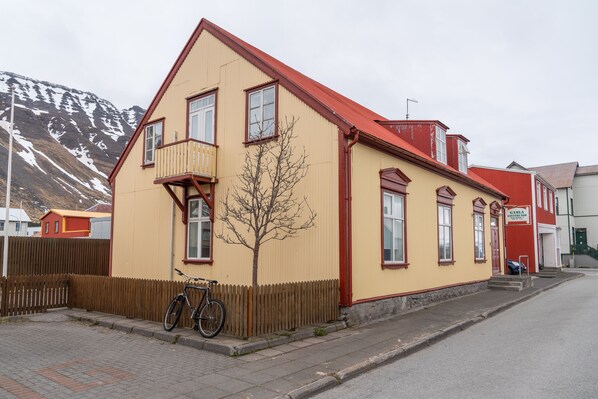 Un edificio de dos plantas con techo rojo y paredes color beige, una valla de madera y una bicicleta estacionada adelante.