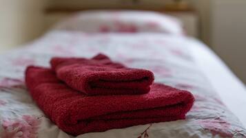 Una cama bien tendida con una colcha de estampado floral y una pila de toallas rojas.