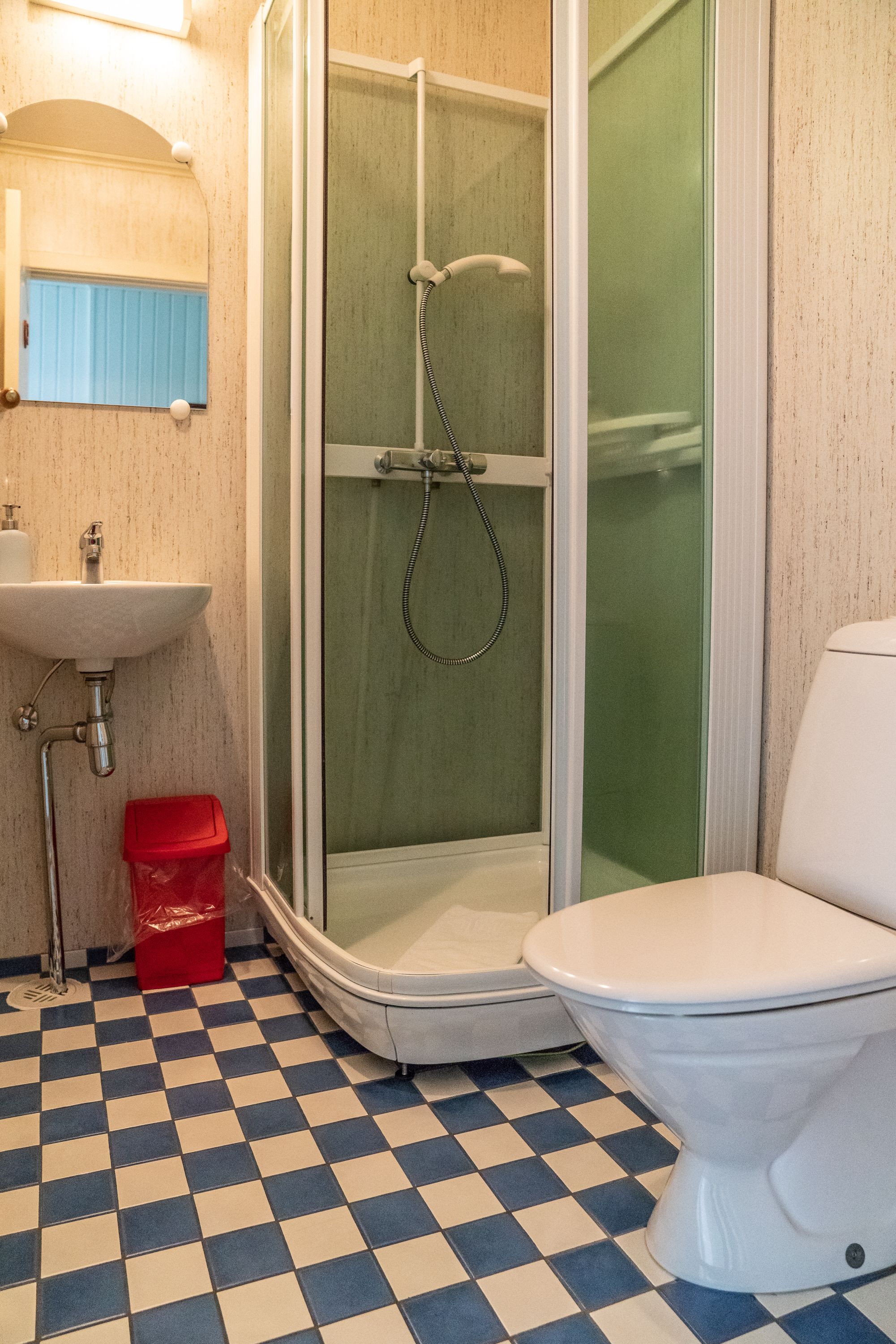A bathroom with a checkered floor, a sink, a toilet, and a glass-enclosed shower.