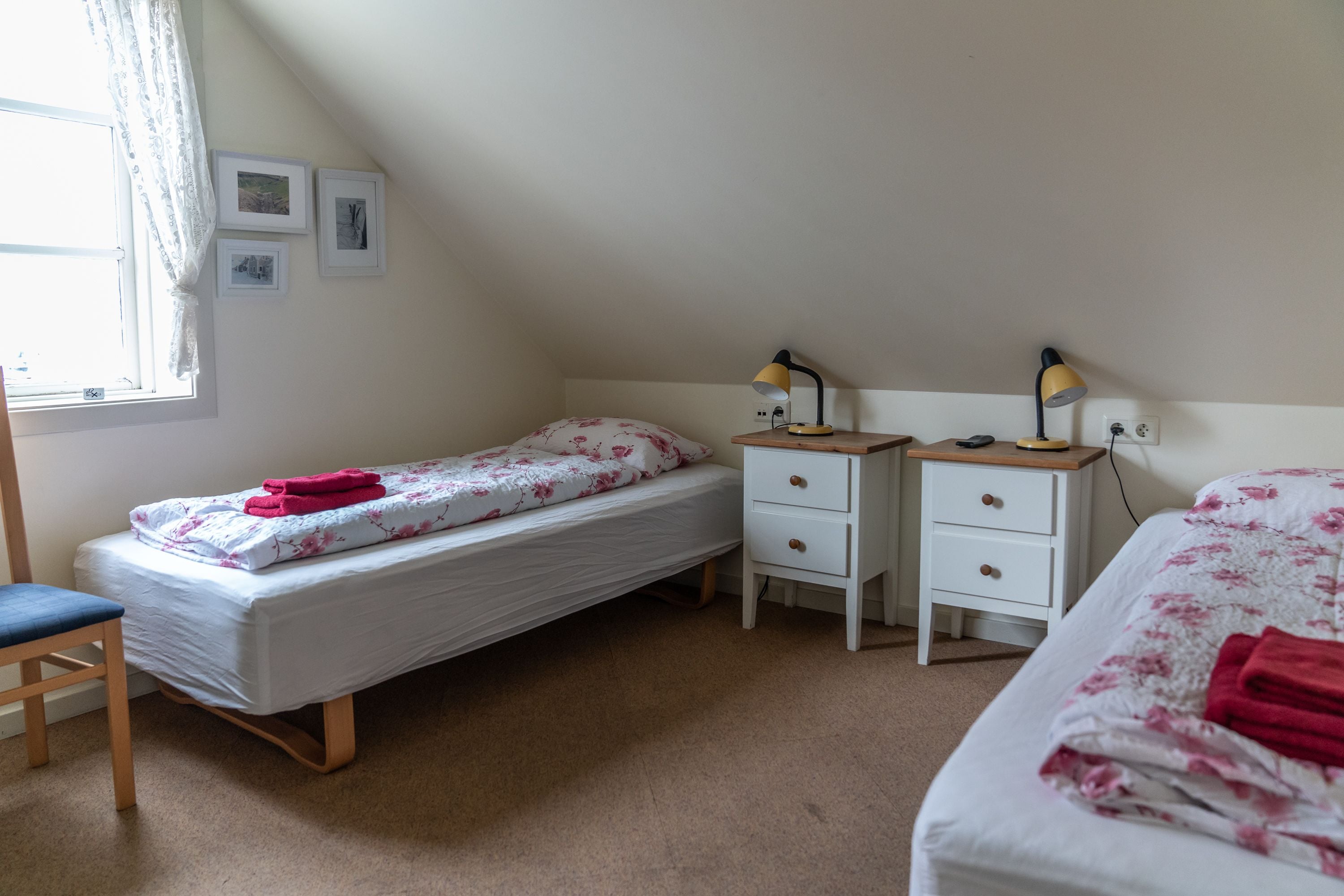 A bedroom with two single beds, a desk, a chair, and a window with curtains.