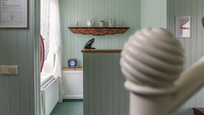 Una habitación con paredes verde claro, un radiador, un estante con adornos y un certificado enmarcado en la pared.