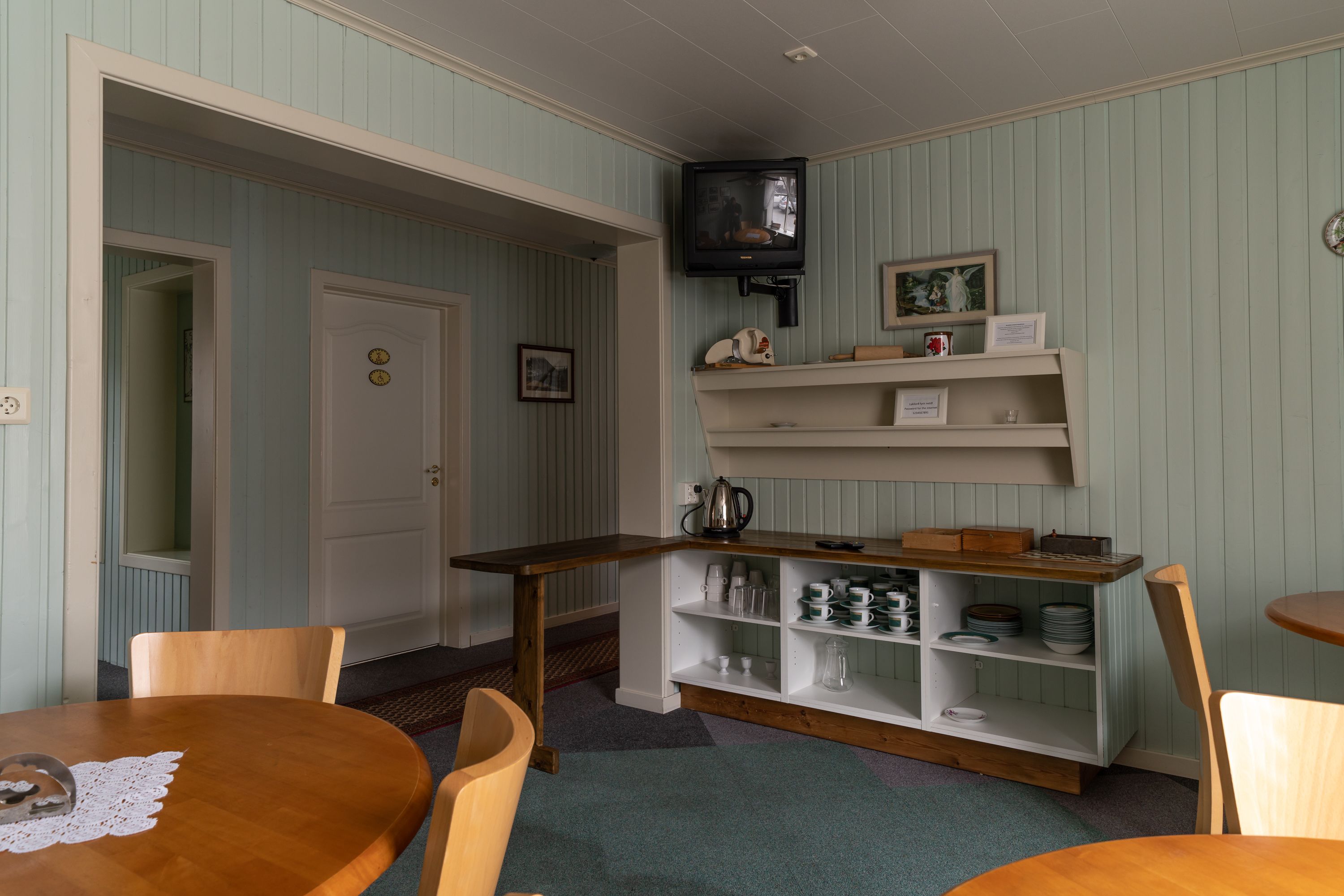 A cozy room with a wooden table, chairs, a television mounted on the wall, and a shelf with various items.