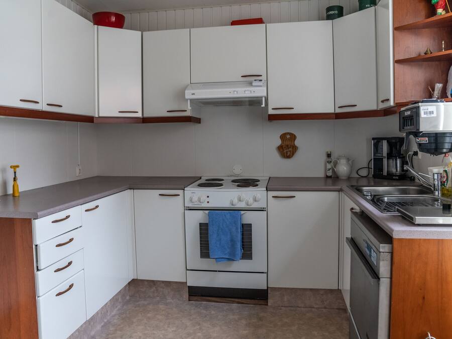 A compact kitchen with white cabinets, a stove, oven, and a coffee maker.