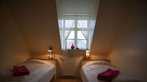 Una habitación pequeña y acogedora con dos camas individuales, una ventana con cortinas translúcidas y un radiador.