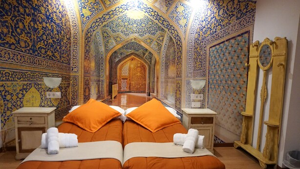 Une pièce avec un mur recouvert de miroirs, un lit avec une literie orange et des motifs complexes bleus et dorés sur les murs et le plafond.