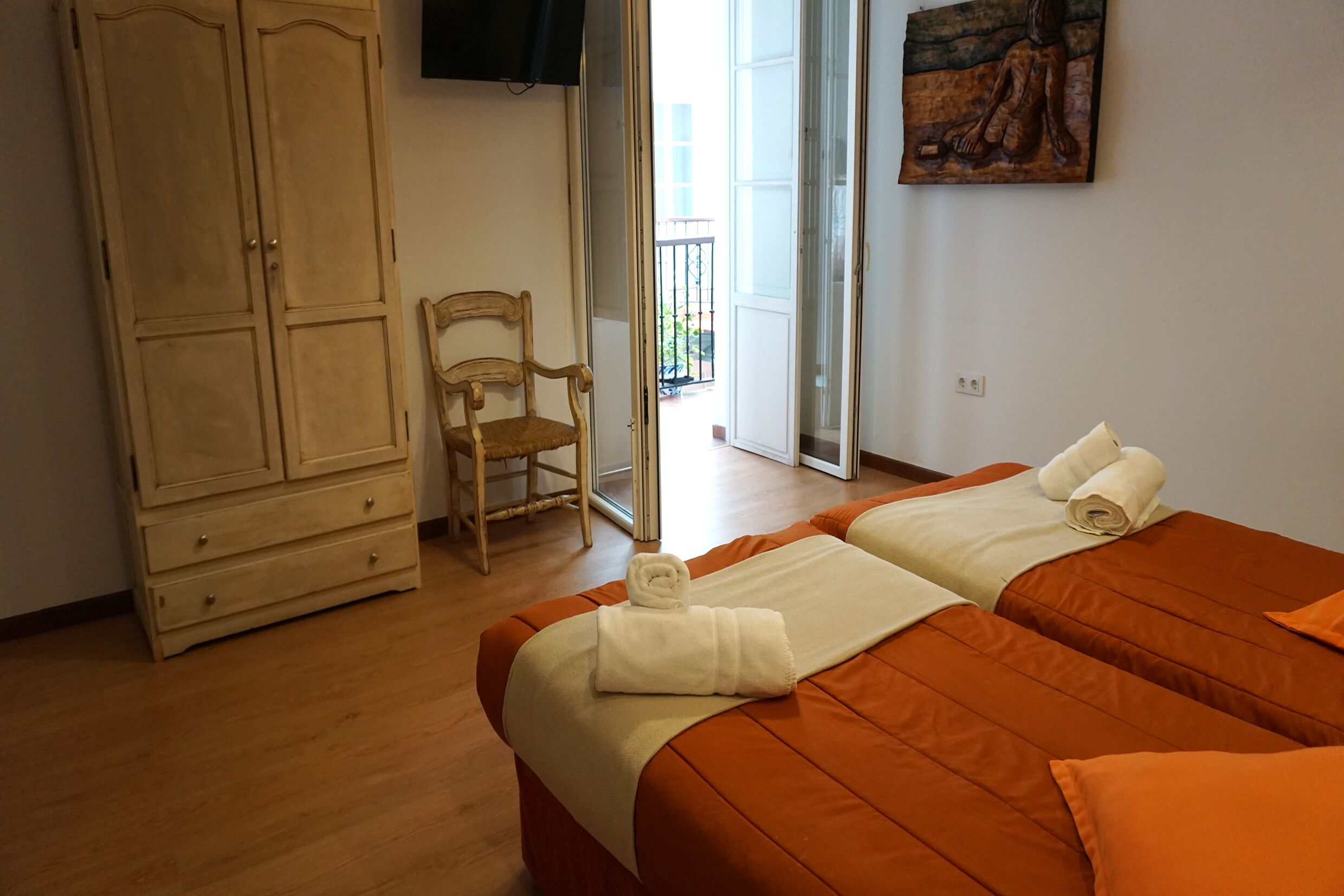 A hotel room with two beds, a wooden wardrobe, a chair, and a painting on the wall.