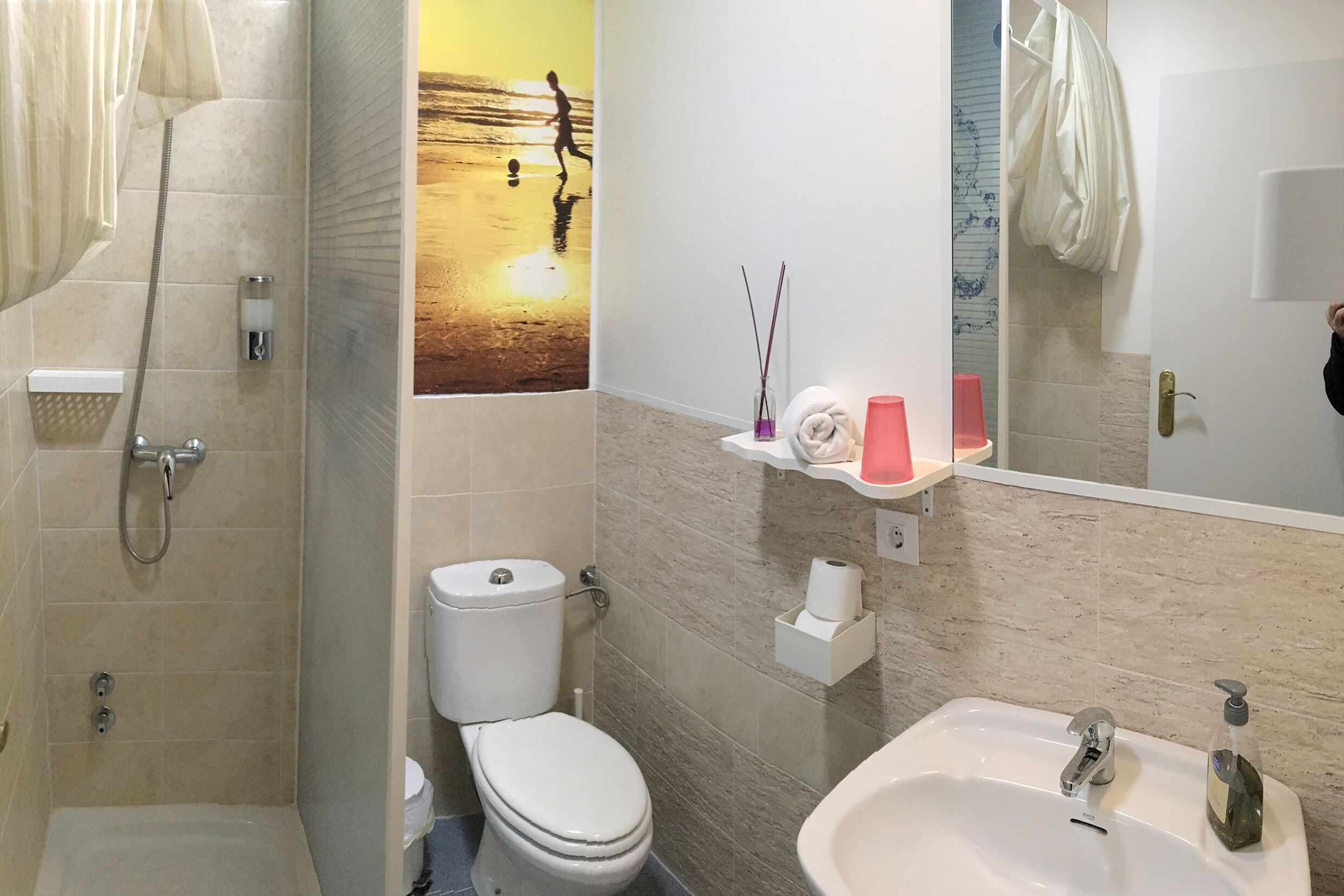 Un baño con ducha, inodoro, lavabo y un espejo instalado en la pared.