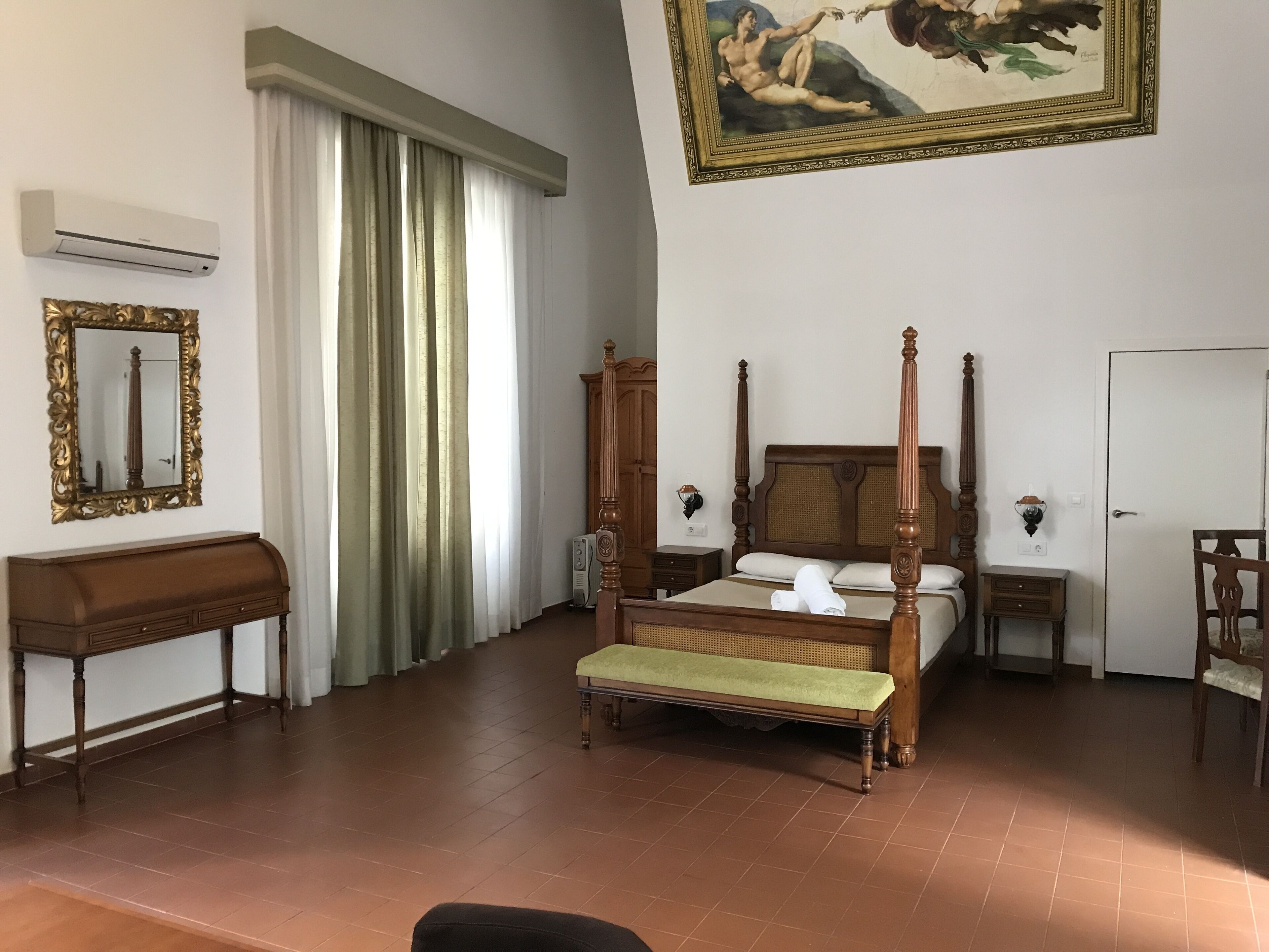 Un dormitorio con cama con dosel, un banco de madera, un escritorio, un espejo y un cuadro en la pared.
