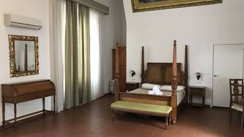 Une chambre à coucher avec un lit à baldaquin, un banc en bois, un bureau, un miroir et un tableau accroché au mur.