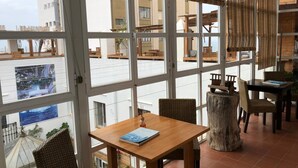 Un vaste espace dédié à la salle à manger, doté de grandes fenêtres, de tables en bois, de chaises en osier et d’un centre de table rustique en forme de tronc d’arbre.