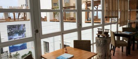 A spacious dining area with large windows, wooden tables, wicker chairs, and a rustic wooden stump centerpiece.