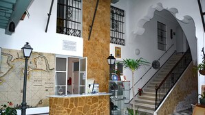 Un hall d’entrée avec un comptoir de réception, une carte, un escalier et des plantes en pot.