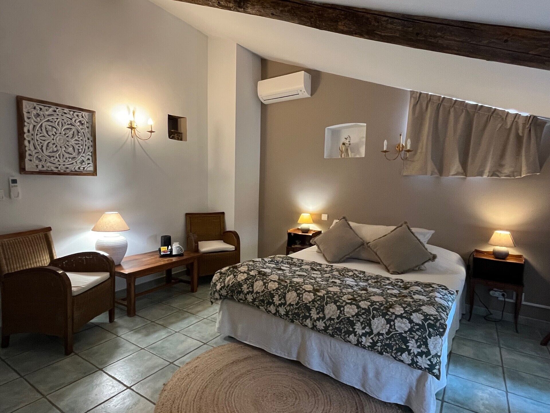 A bedroom with a bed, two bedside tables, a chair, a lamp, and a wall-mounted air conditioner.