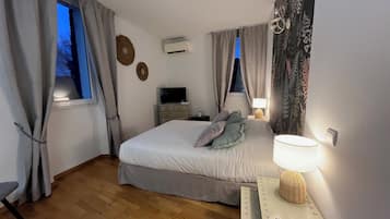 Un dormitorio con cama, televisión, lámpara y ventana con cortinas.