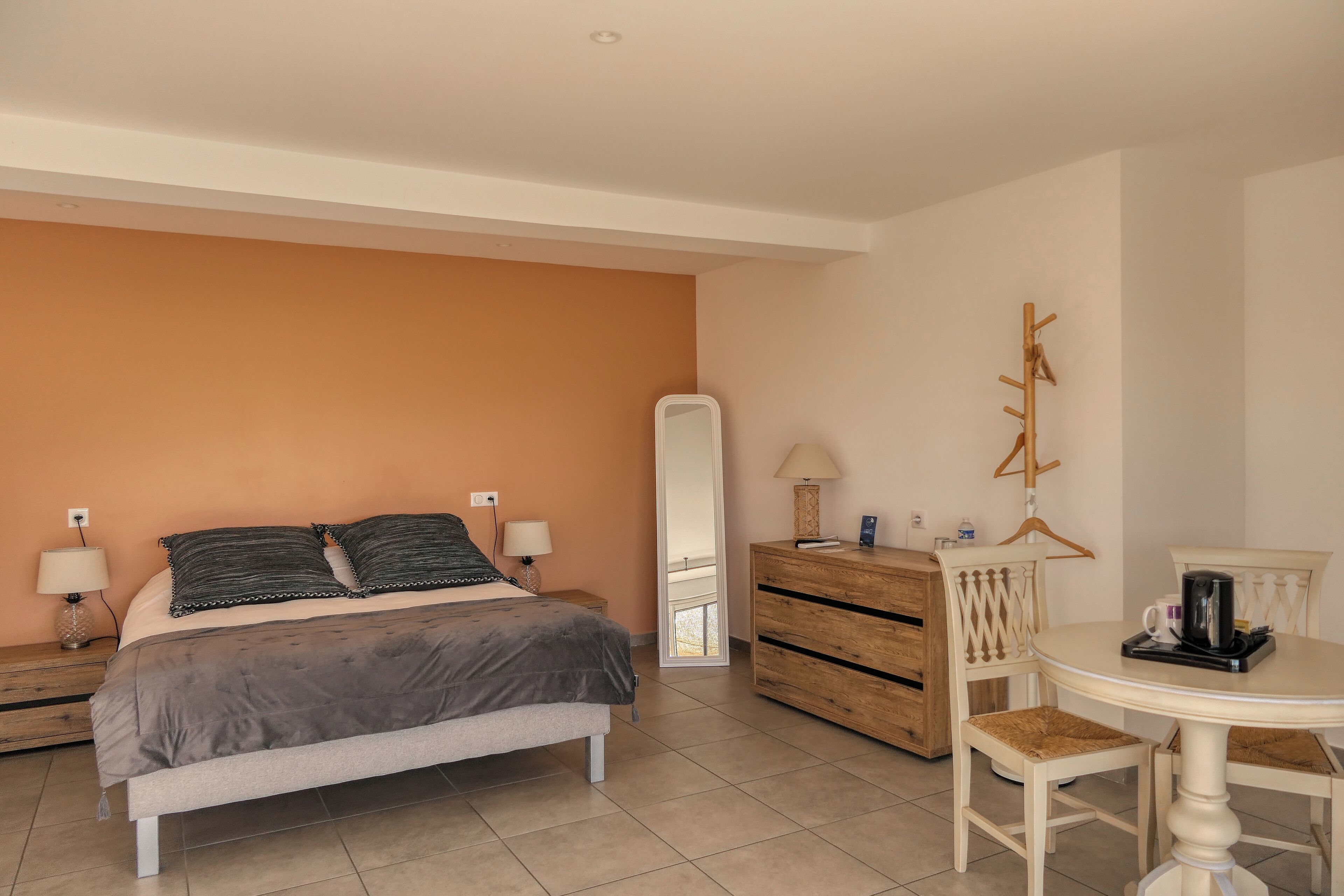 Un dormitorio con cama, cómoda, espejo y una pequeña mesa redonda con una silla.