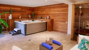 Zona de spa con hidromasaje, paredes de madera, puerta de cristal que da a un balcón y una sala de estar con una toalla y un objeto decorativo.