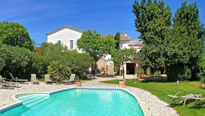 Una piscina con sillas de descanso, rodeada de exuberante vegetación y un edificio blanco al fondo.