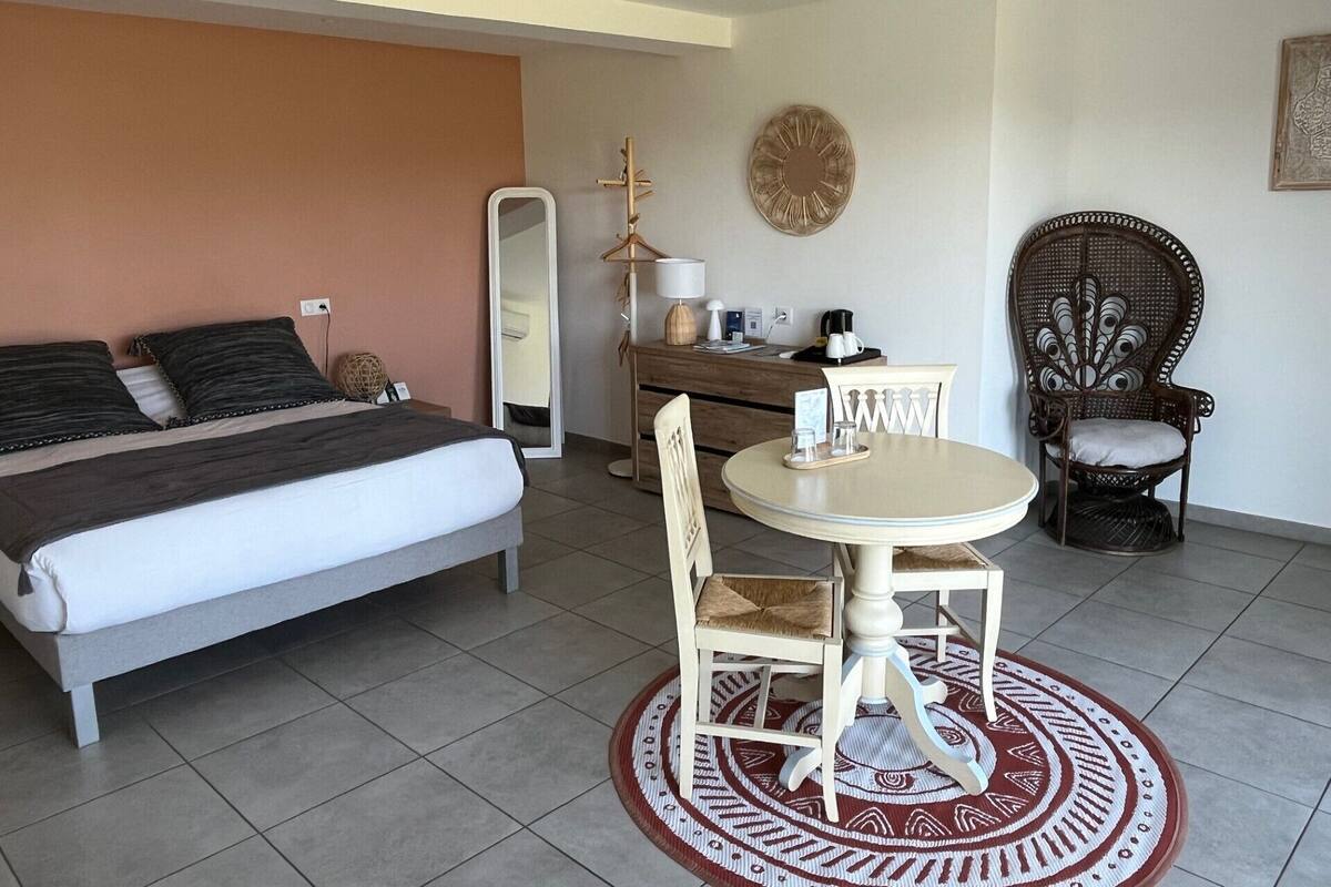 Een slaapkamer met een bed, een dressoir, een ronde eettafel met stoelen, een spiegel en een decoratief object aan de muur.