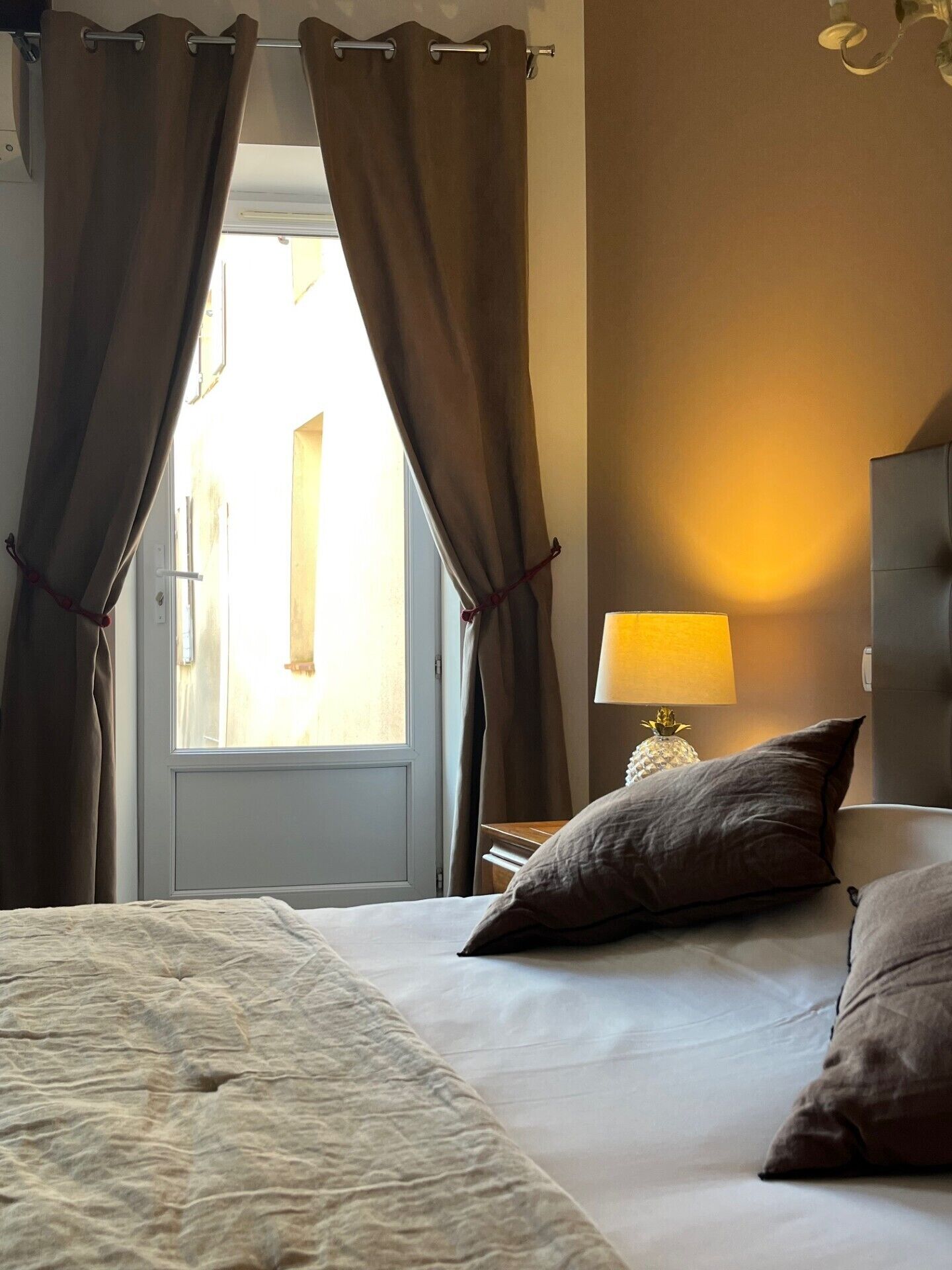 A hotel room with a bed, curtains, a lamp, and a view through the window.