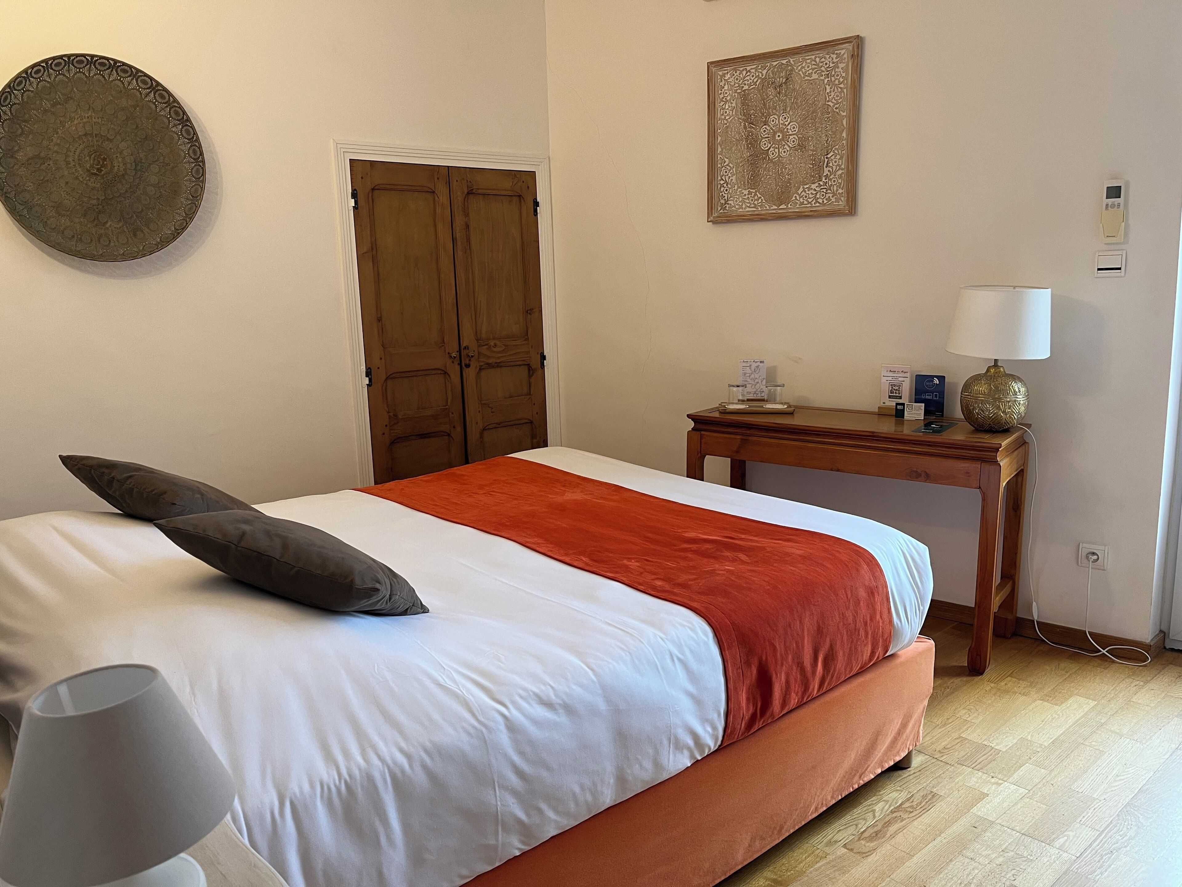 Un dormitorio ordenado con una cama, una mesita de noche con lámpara y una puerta.