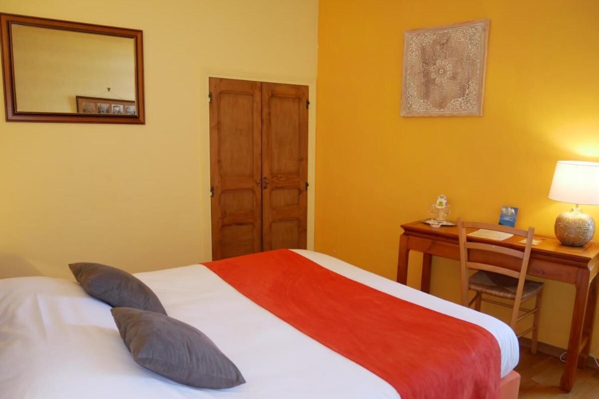 Une chambre d’hôtel avec un lit, un bureau, une chaise, une lampe, un miroir et une porte.