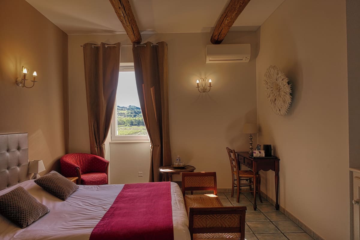 Een hotelkamer met een bed, een rode fauteuil, een houten bureau en uitzicht op de omgeving.